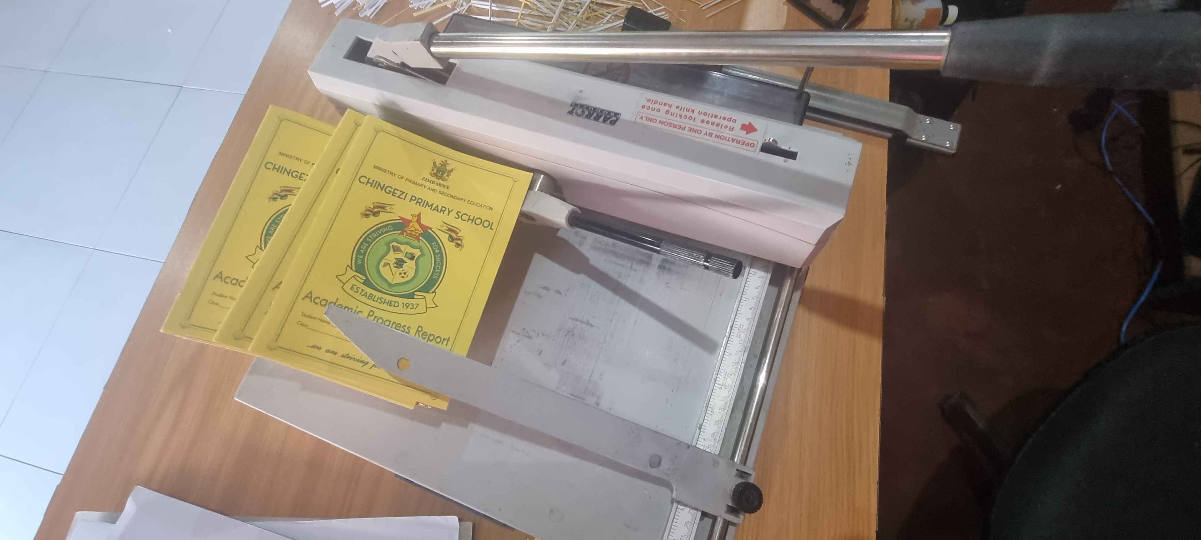 Printed academic progress report booklets with a school crest, being trimmed on a guillotine