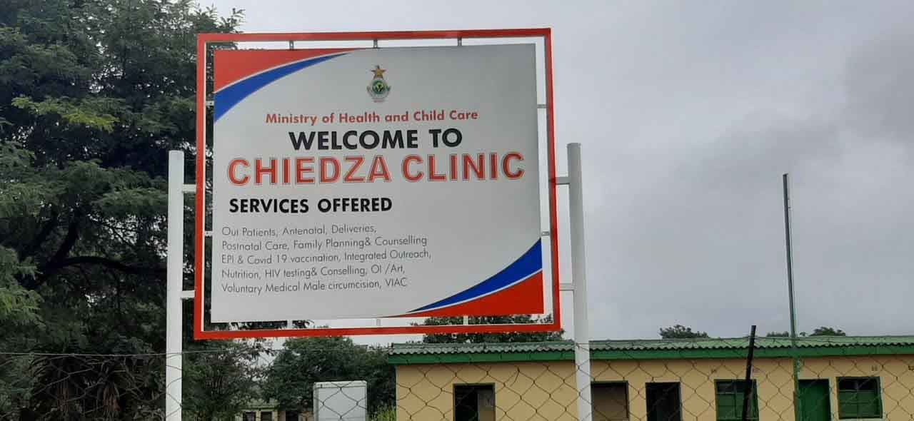A clinic welcome board listing the services offered, mounted on steel posts at the facility entrance
