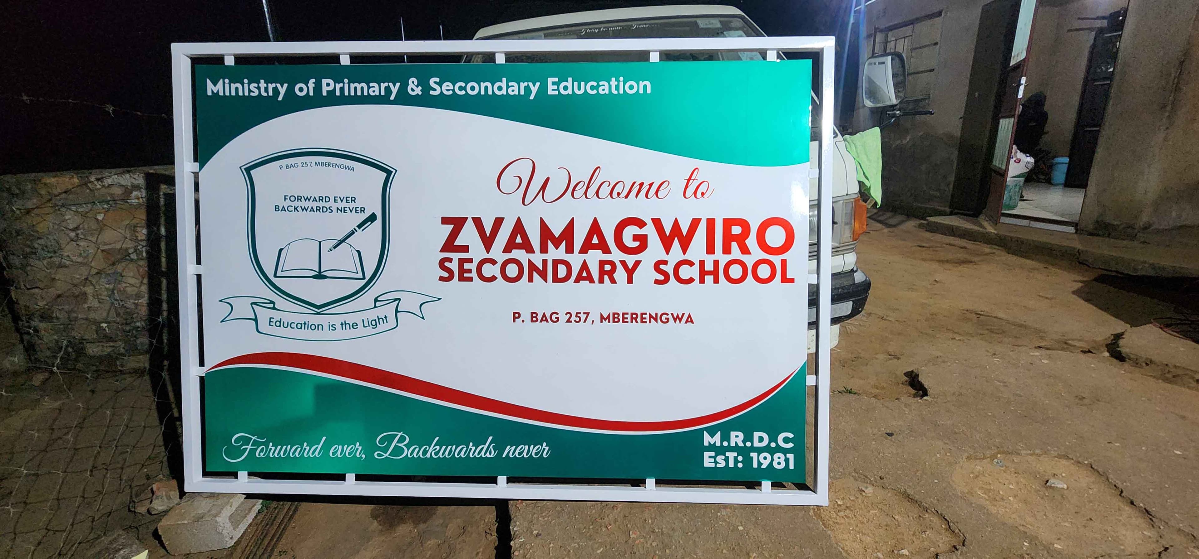 A secondary school welcome sign with crest, and a distance and arrow, in teal, white and red